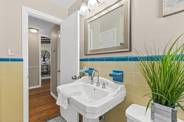 bathroom featuring tile walls, toilet, a wainscoted wall, a sink, and wood finished floors