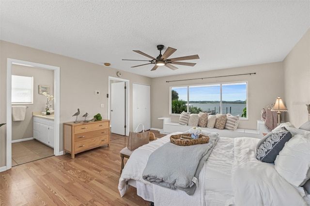 bedroom with light wood-type flooring, baseboards, a textured ceiling, connected bathroom, and ceiling fan