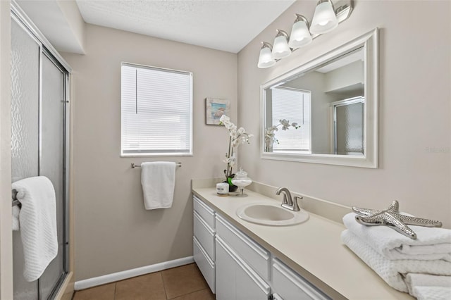 bathroom with vanity, baseboards, a textured ceiling, a shower stall, and tile patterned floors