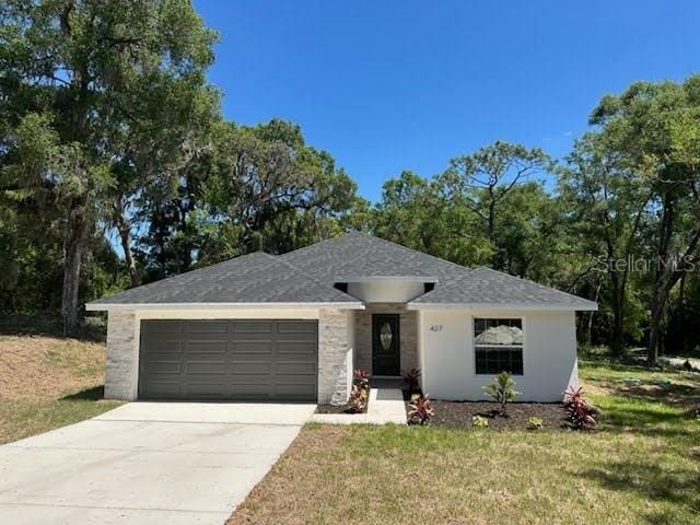single story home featuring roof with shingles, stucco siding, driveway, an attached garage, and a front lawn