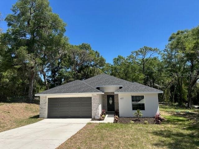 ranch-style home featuring an attached garage, driveway, a front yard, and stucco siding