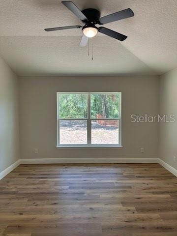 unfurnished room featuring ceiling fan, a textured ceiling, vaulted ceiling, wood finished floors, and baseboards
