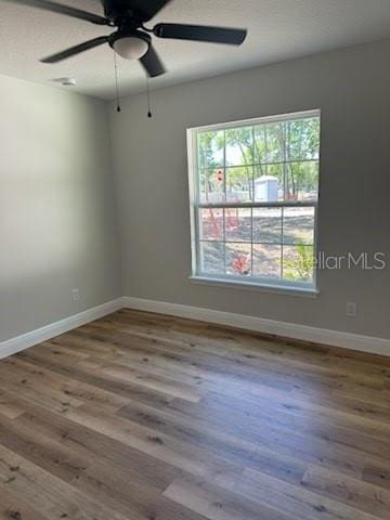 empty room with ceiling fan, baseboards, wood finished floors, and a healthy amount of sunlight