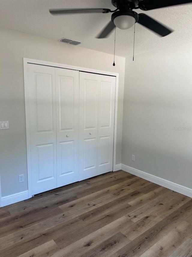 unfurnished bedroom featuring a closet, a ceiling fan, visible vents, wood finished floors, and baseboards
