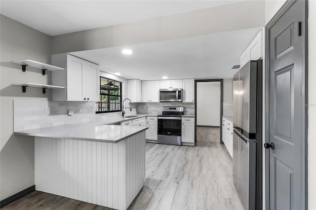 kitchen featuring tasteful backsplash, a sink, light wood-style flooring, a peninsula, and appliances with stainless steel finishes