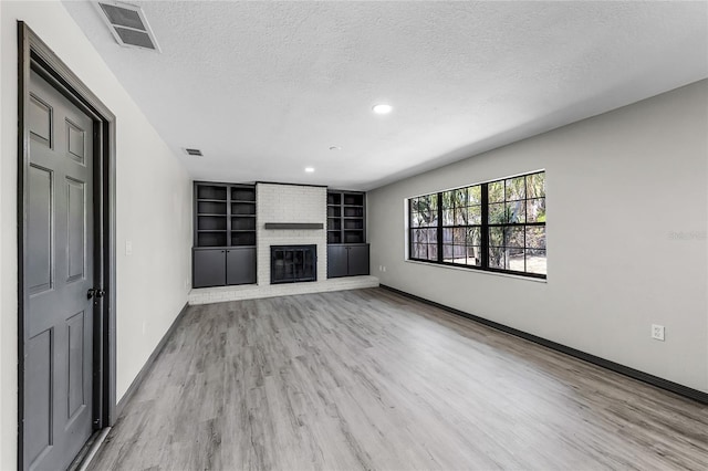 unfurnished living room with a textured ceiling, visible vents, light wood finished floors, baseboards, and a fireplace