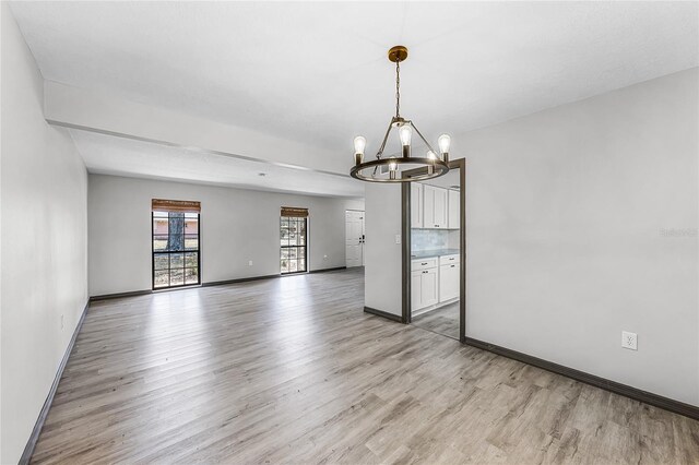 spare room with baseboards, an inviting chandelier, and light wood-style floors