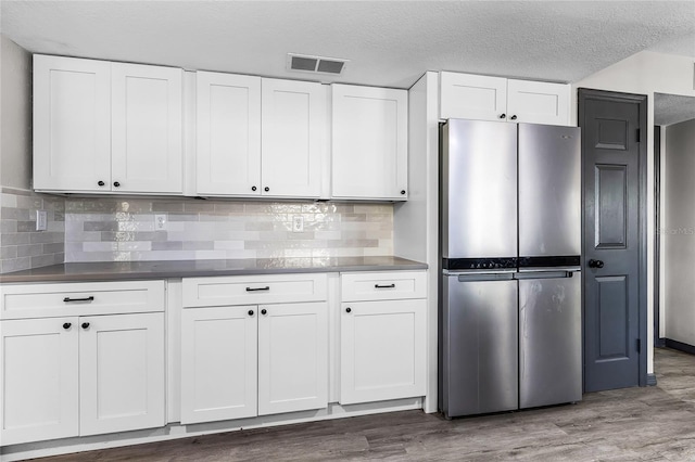 kitchen with white cabinetry, tasteful backsplash, dark wood-style flooring, visible vents, and freestanding refrigerator