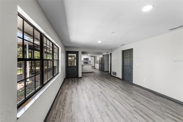 unfurnished living room with a wealth of natural light, visible vents, and wood finished floors