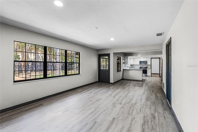 unfurnished living room featuring recessed lighting, baseboards, a textured ceiling, light wood finished floors, and visible vents