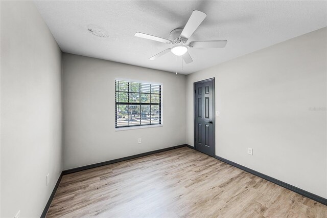 empty room featuring baseboards, a textured ceiling, a ceiling fan, and light wood finished floors