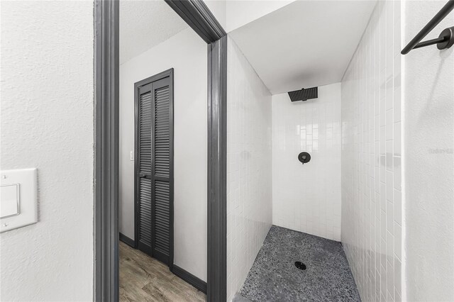 full bath featuring wood finished floors, tiled shower, and a textured wall