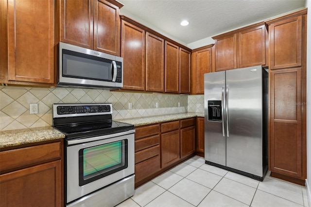 8639 Lower Villagewalk Cir, Orlando, FL 32827 - kitchen with stainless steel appliances, light tile patterned floors, light stone countertops, tasteful backsplash, and brown cabinetry