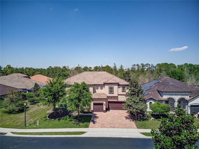 mediterranean / spanish house with a front yard, a tiled roof, an attached garage, stucco siding, and decorative driveway