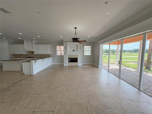 unfurnished living room with baseboards, ornamental molding, a tiled fireplace, a ceiling fan, and visible vents