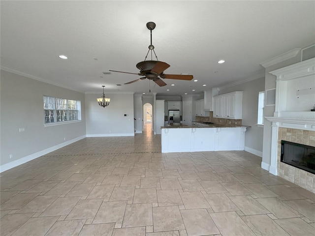 unfurnished living room featuring baseboards, a tiled fireplace, ceiling fan with notable chandelier, and ornamental molding