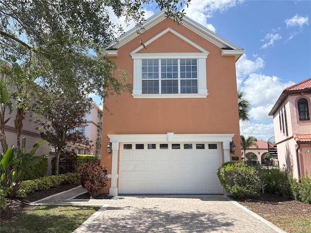 traditional-style home with decorative driveway, a garage, and stucco siding