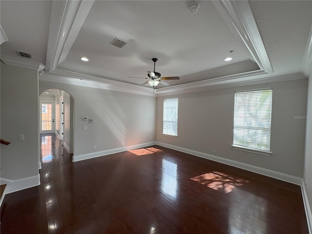 unfurnished room featuring dark wood-style floors, arched walkways, ceiling fan, and a raised ceiling