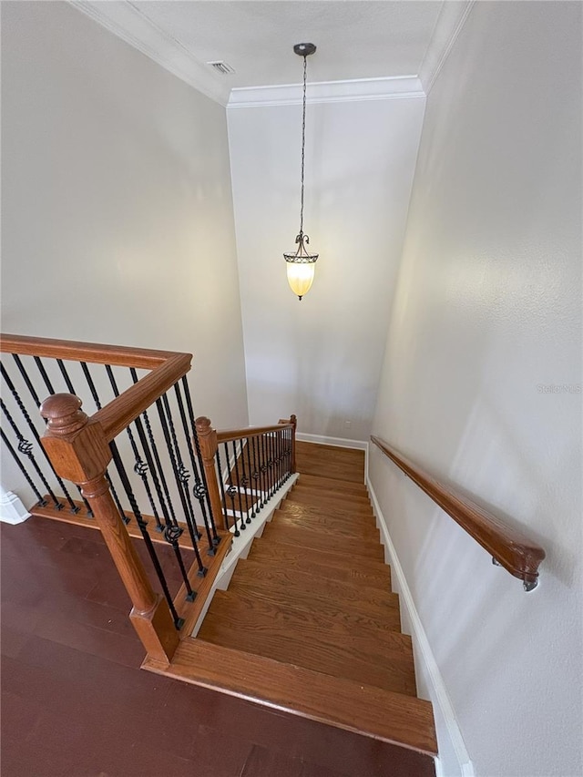 staircase with wood finished floors, baseboards, ornamental molding, and visible vents