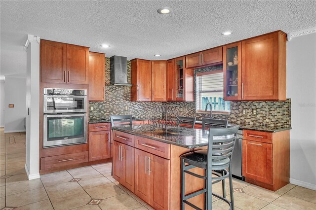 kitchen with dark stone countertops, light tile patterned floors, a center island, stainless steel double oven, and wall chimney exhaust hood
