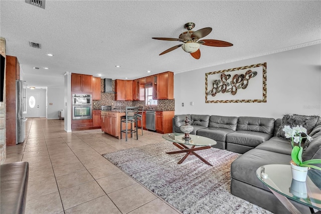living area with light tile patterned floors, visible vents, a textured ceiling, and ceiling fan