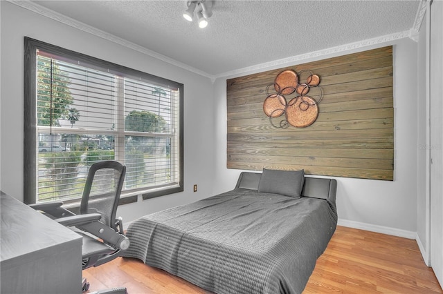 bedroom featuring ornamental molding, baseboards, wood finished floors, and a textured ceiling