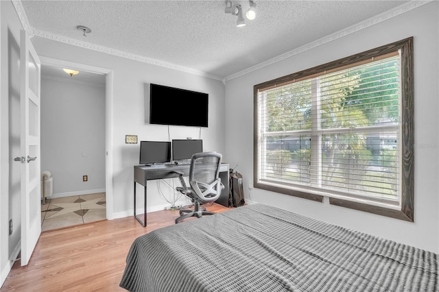 bedroom featuring light wood-style flooring, a textured ceiling, and ornamental molding
