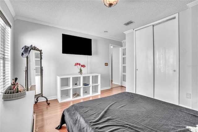 bedroom featuring a textured ceiling, a closet, ornamental molding, visible vents, and wood finished floors