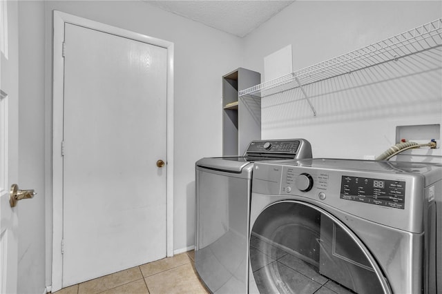 clothes washing area with washer and dryer, laundry area, light tile patterned flooring, and a textured ceiling