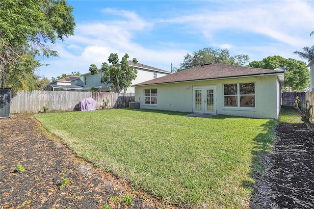rear view of house with stucco siding, french doors, a fenced backyard, a yard, and a shingled roof
