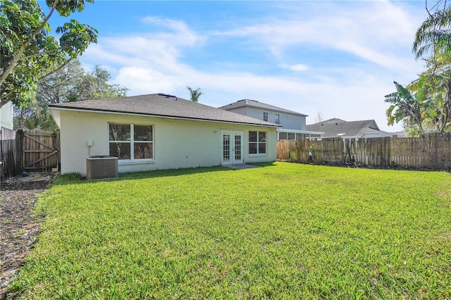 rear view of house with stucco siding, french doors, cooling unit, a fenced backyard, and a lawn