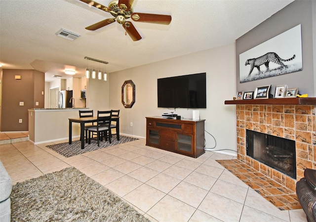 living room with a textured ceiling, visible vents, a tile fireplace, ceiling fan, and light tile patterned floors