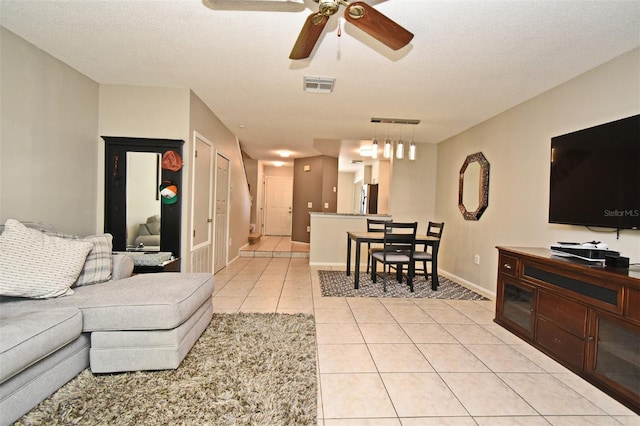 living room featuring light tile patterned flooring, a textured ceiling, visible vents, and a ceiling fan