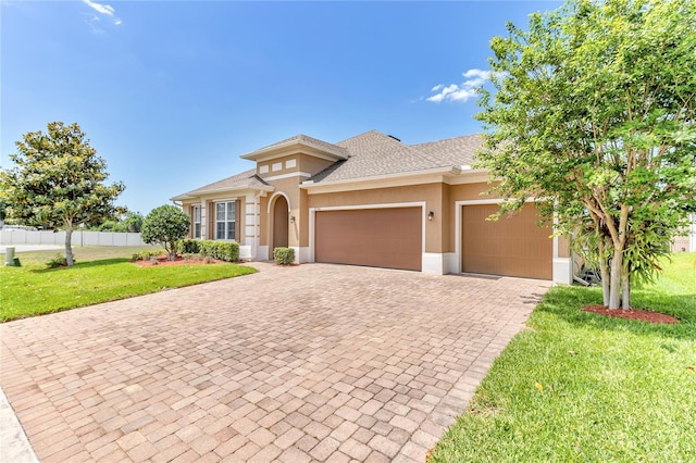 mediterranean / spanish-style house with fence, a garage, a front yard, stucco siding, and decorative driveway