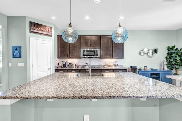 2724 Westyn Cove Ln, Ocoee, FL 34761 - kitchen featuring stainless steel microwave, a sink, dark brown cabinets, backsplash, and a center island with sink