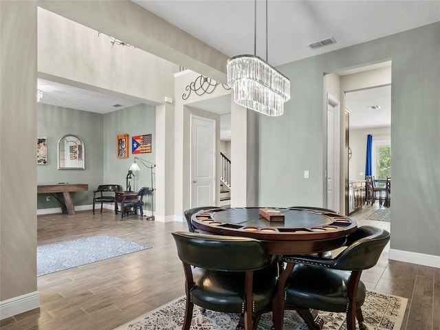 dining area featuring an inviting chandelier, wood finished floors, visible vents, baseboards, and stairs