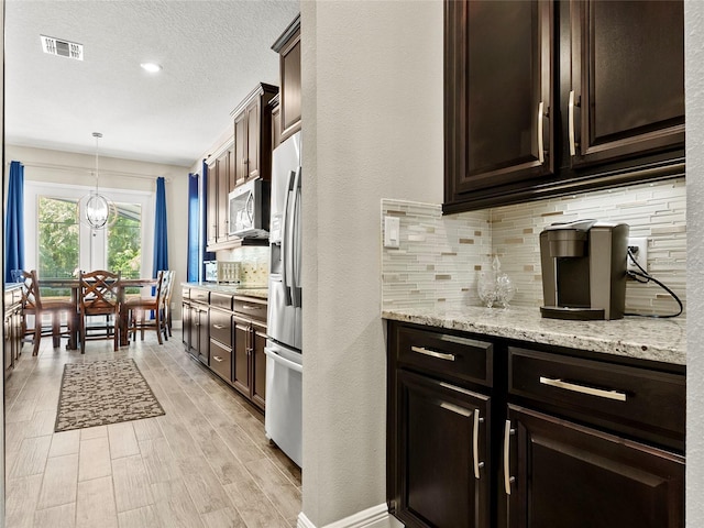 kitchen featuring stainless steel appliances, dark brown cabinets, visible vents, backsplash, and light stone countertops