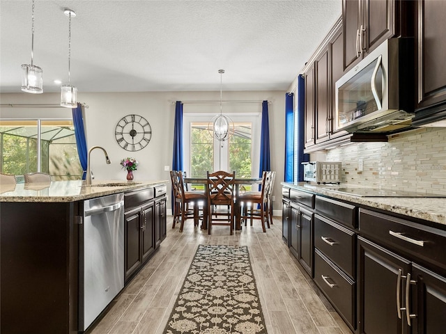 kitchen featuring a sink, tasteful backsplash, light wood-style floors, pendant lighting, and appliances with stainless steel finishes