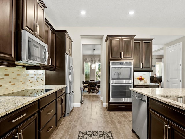 kitchen with light stone counters, dark brown cabinets, light wood-type flooring, and stainless steel appliances