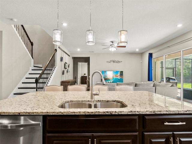 kitchen with dishwasher, a sink, dark brown cabinetry, open floor plan, and ceiling fan