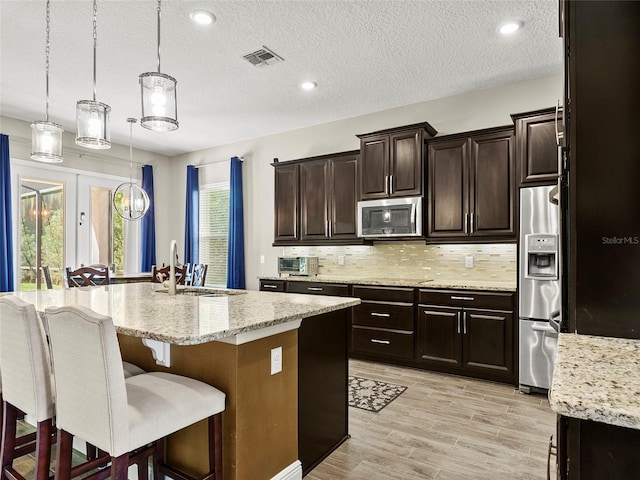 kitchen with stainless steel appliances, a sink, visible vents, backsplash, and a breakfast bar