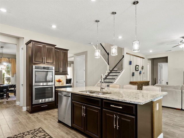 kitchen featuring an island with sink, stainless steel appliances, a sink, light wood-style floors, and open floor plan