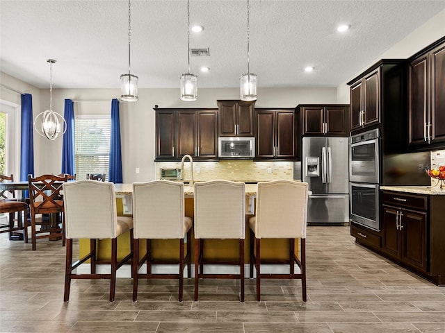 kitchen featuring decorative backsplash, stainless steel appliances, a textured ceiling, and a kitchen bar
