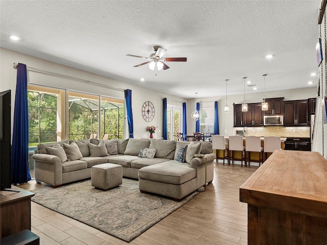 living area featuring recessed lighting, light wood-type flooring, a textured ceiling, and a ceiling fan