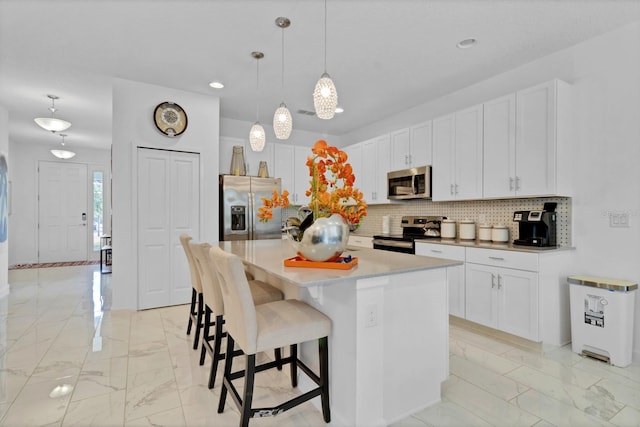 kitchen with white cabinetry, a kitchen bar, stainless steel appliances, backsplash, and marble finish floor
