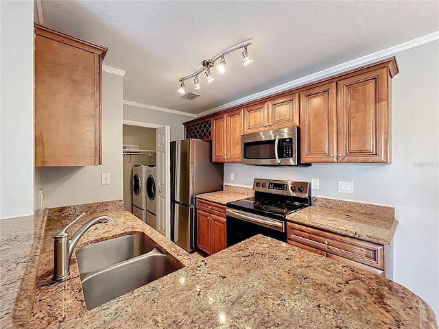kitchen featuring ornamental molding, appliances with stainless steel finishes, light stone counters, brown cabinetry, and washer and clothes dryer