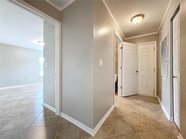 hallway featuring baseboards, ornamental molding, and light tile patterned floors