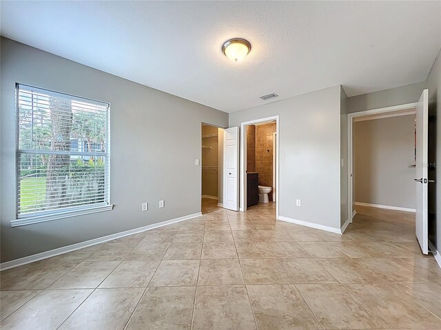unfurnished bedroom featuring a spacious closet, ensuite bathroom, light tile patterned floors, baseboards, and visible vents