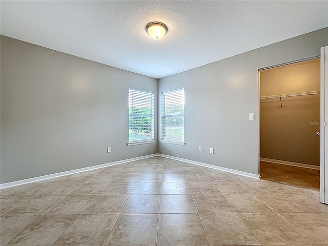 empty room with baseboards, a textured ceiling, and light tile patterned floors