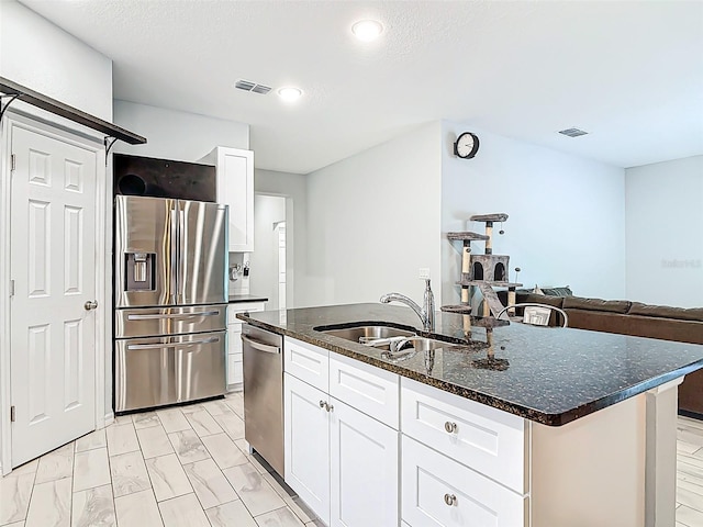 kitchen featuring dark stone countertops, a sink, appliances with stainless steel finishes, visible vents, and a center island with sink